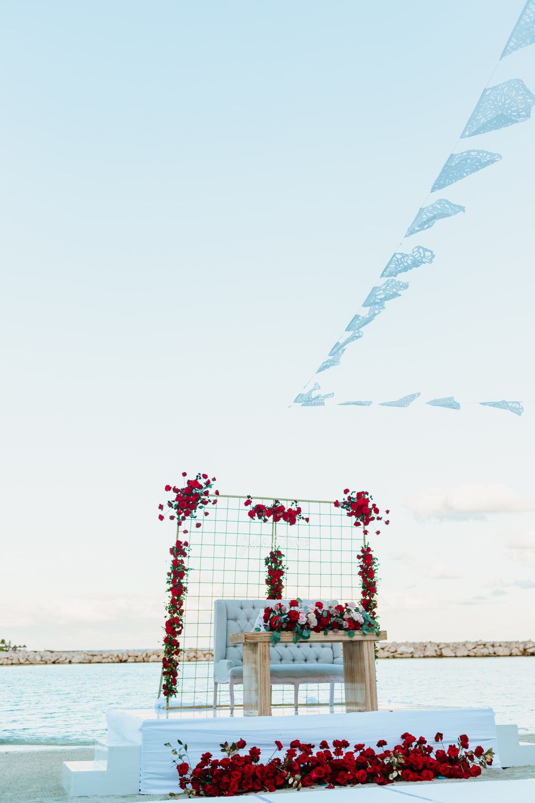 Sweetheart table under a rose-dressed grid, papel picado against the sky