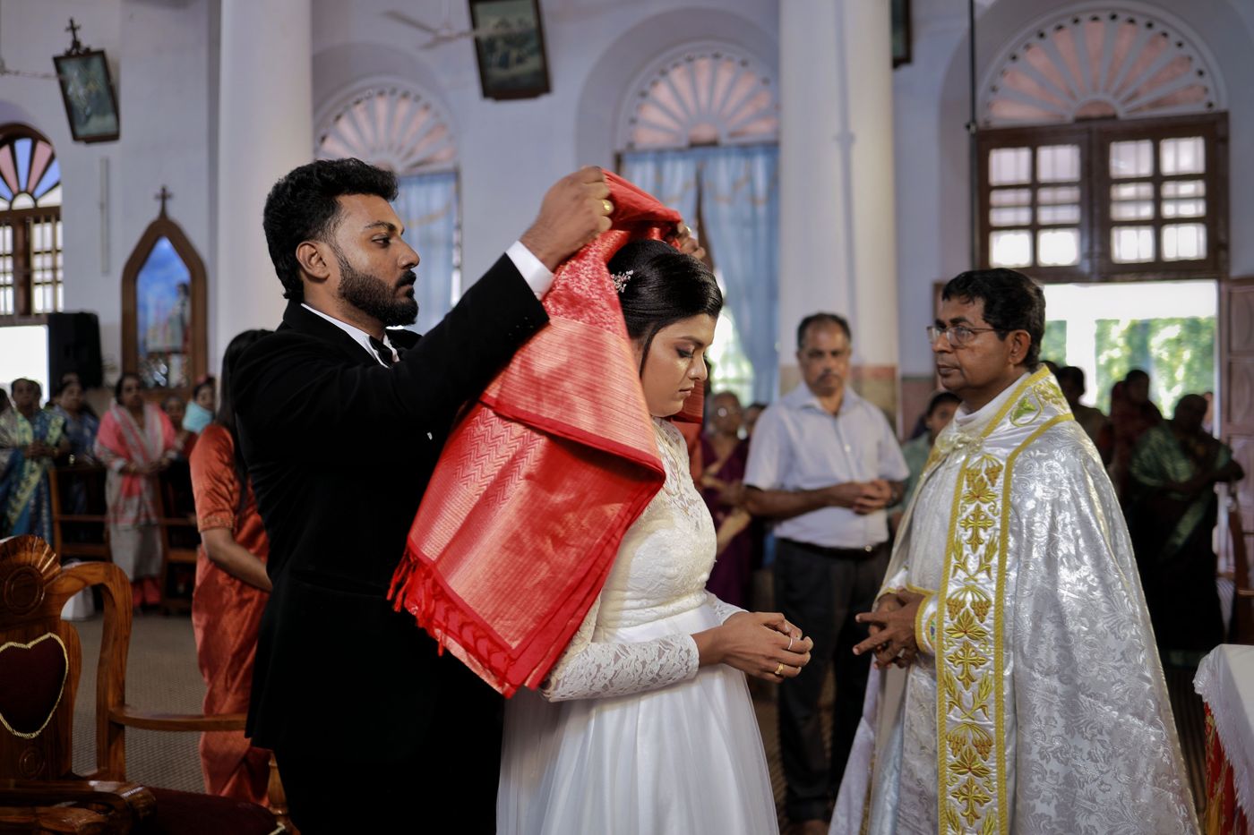 The groom placing the manthrakodi on the bride before the priest at a Kerala church wedding