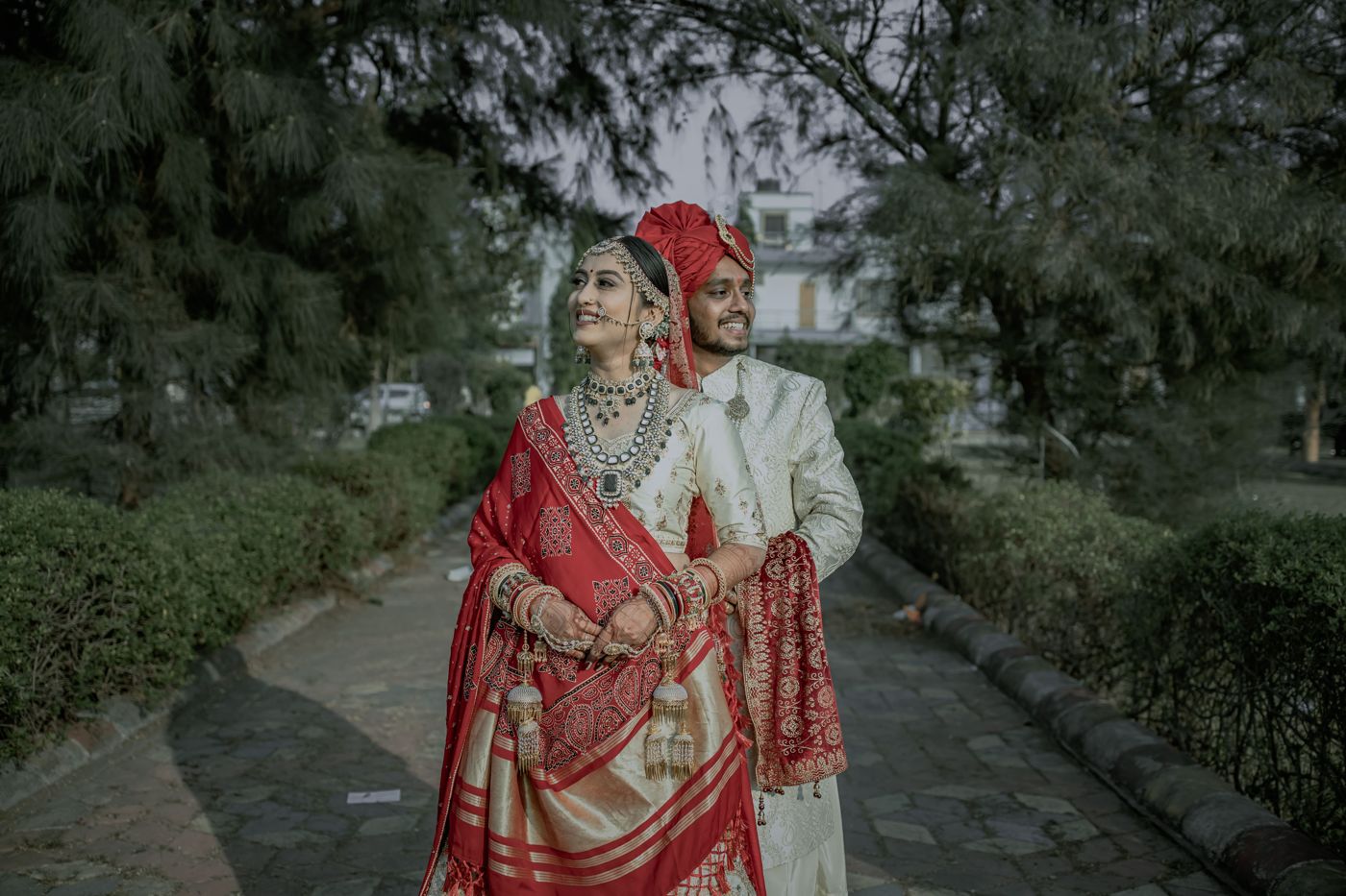 A bride in a cream and red sari with a block-printed odhni beside her groom in a red safa