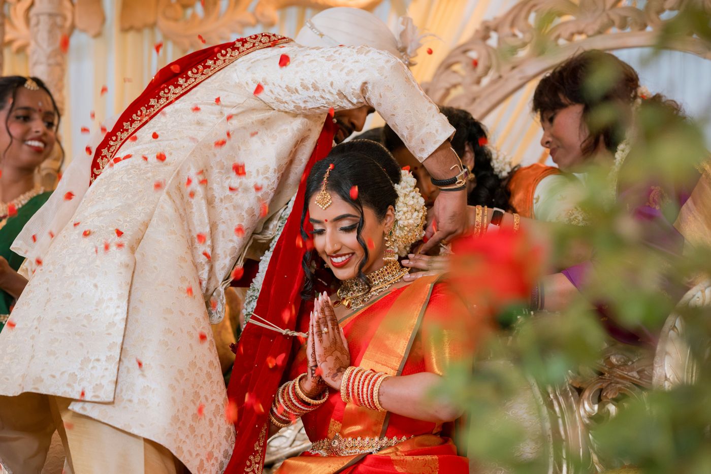 The thaali being tied as petals fall over a bride in red silk and jasmine